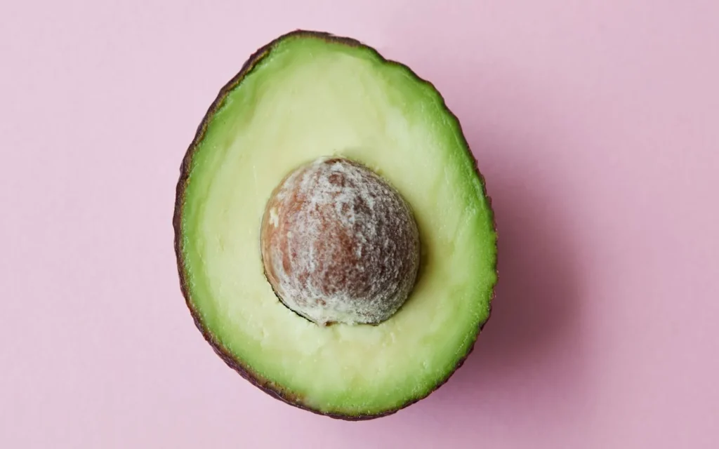 Aguacate abierto sobre fondo rosa