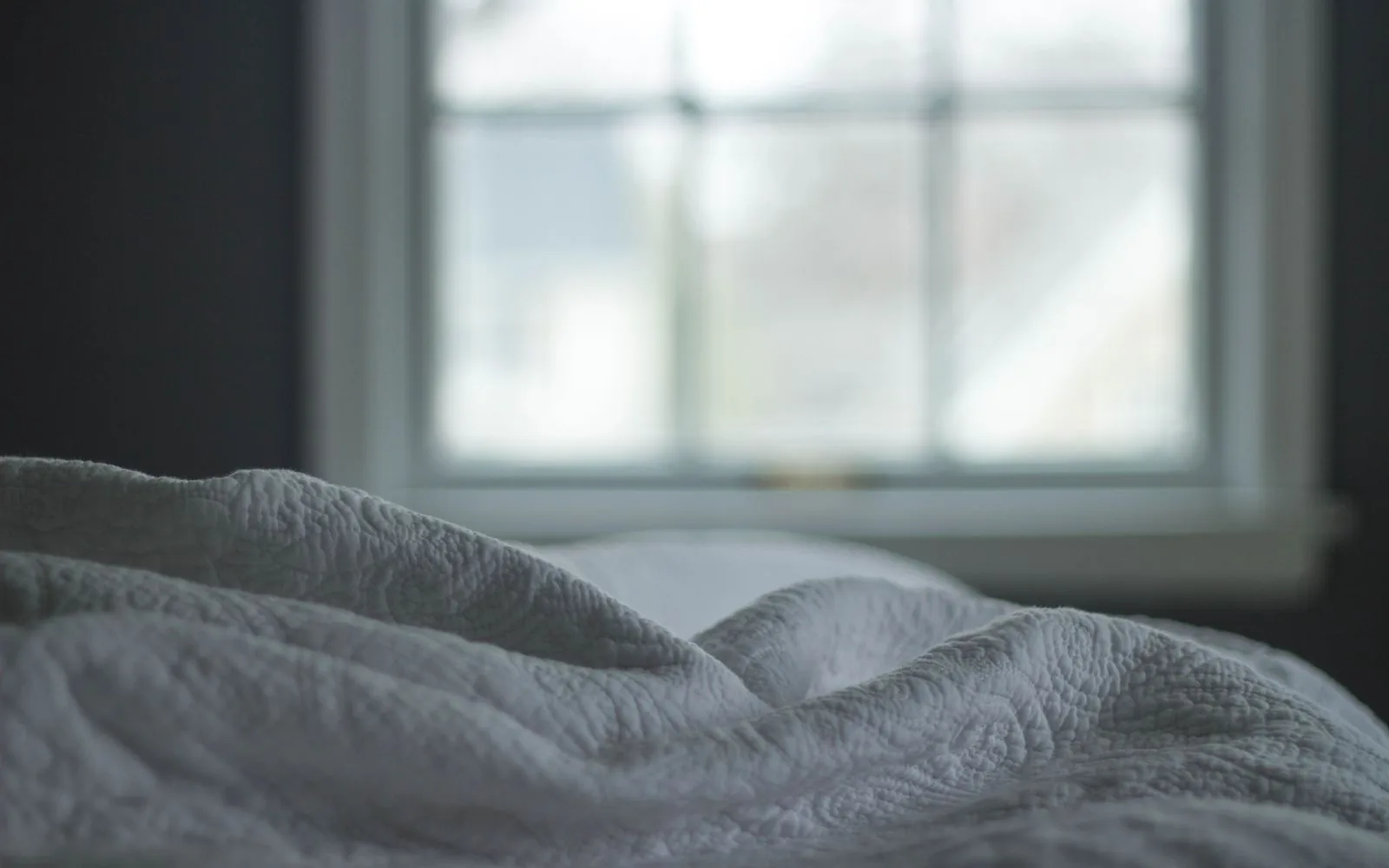 Cama con ropa de cama gris junto a una ventana