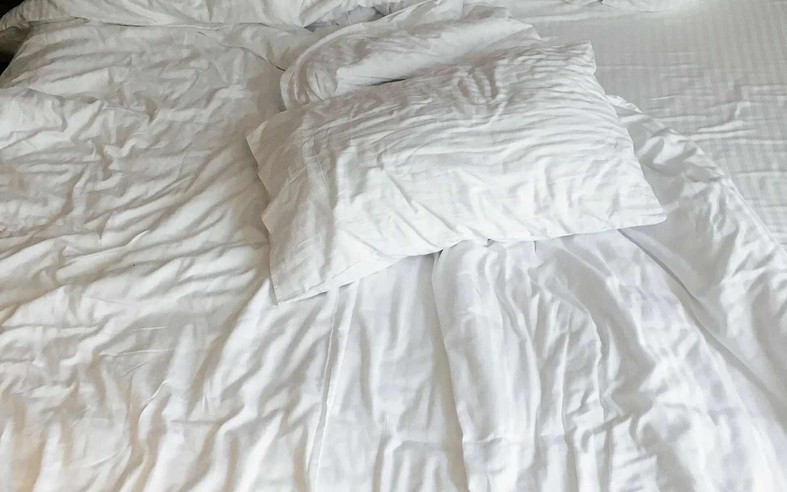 Cama con almohada y sábanas blancas